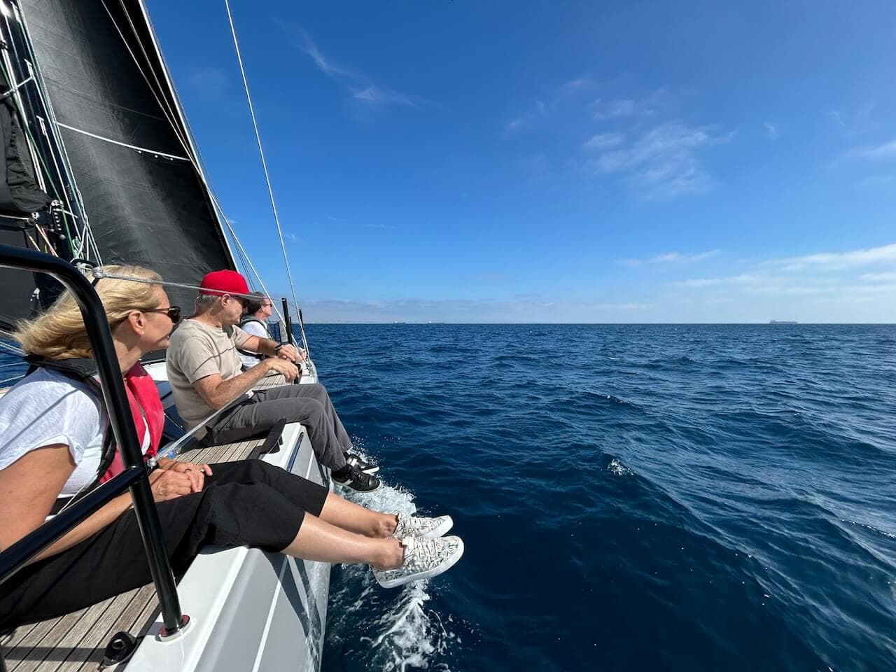 Group of people sitting on the side of a boat with their legs hanging off the side as they charter a boat in Marina del Rey