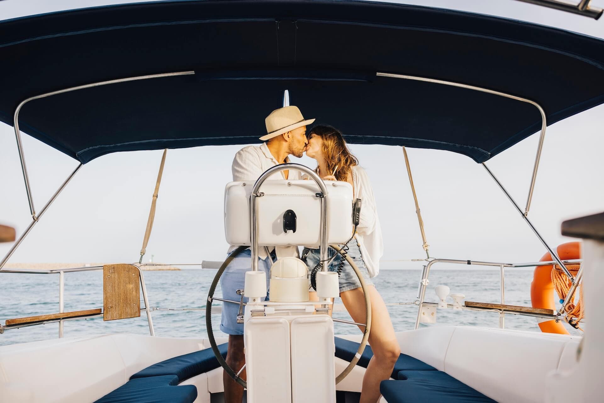A couple embraces and kisses on a boat during a sunny day, symbolizing romance, travel, and leisure on the open sea.