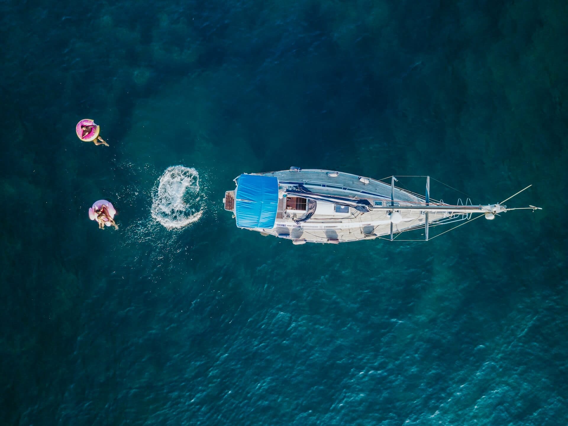 Aerial view of individuals enjoying a leisurely swim next to a moored boat in clear blue waters