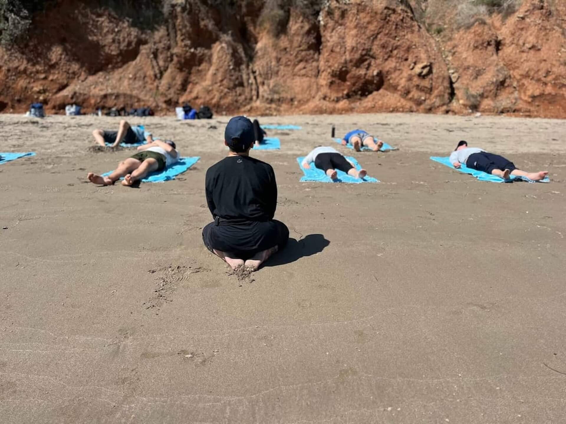 Yoga instructor leading a class on the sandy beach beside a yacht