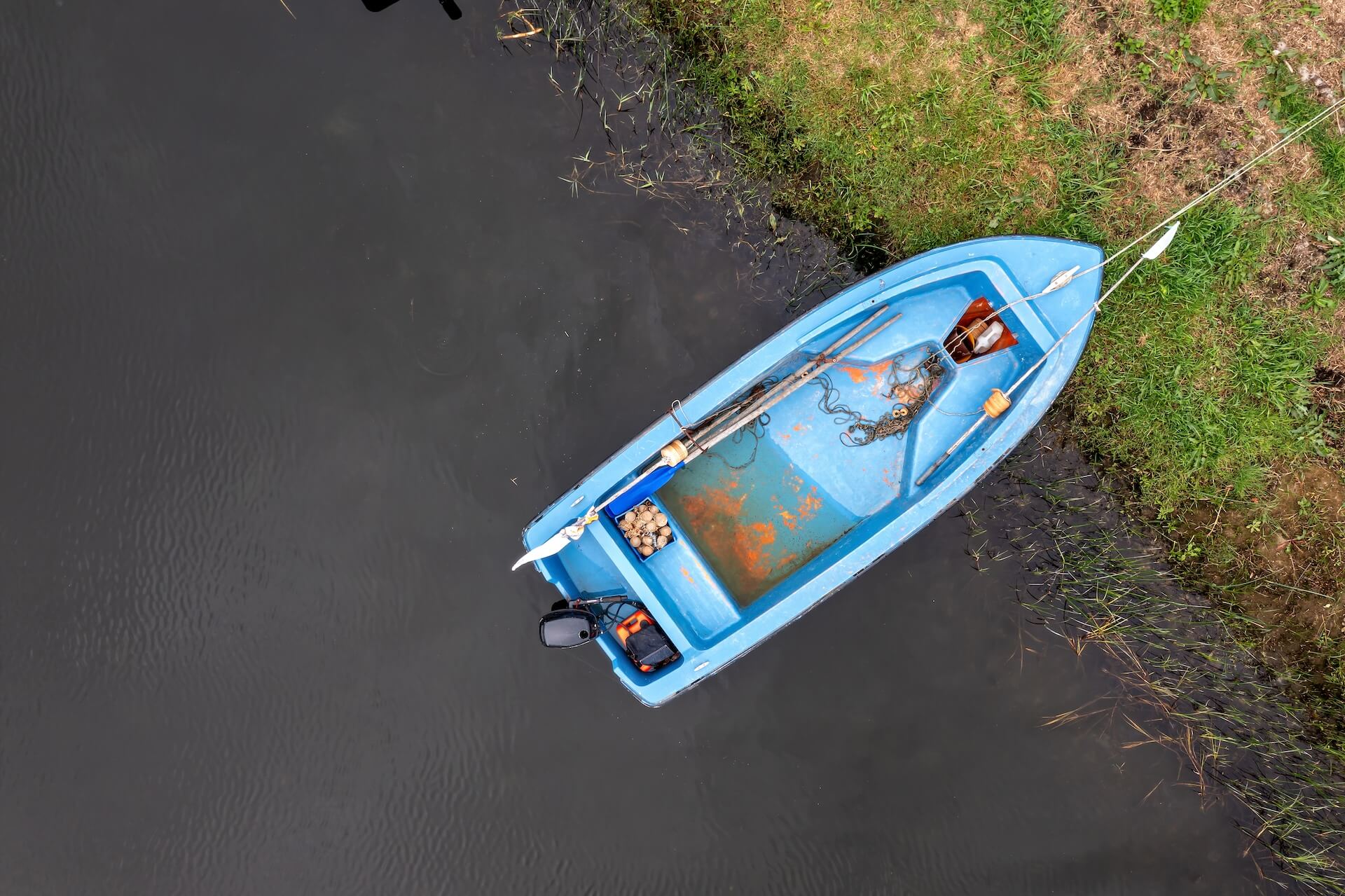 a blue fishing boat anchored by the riverbank