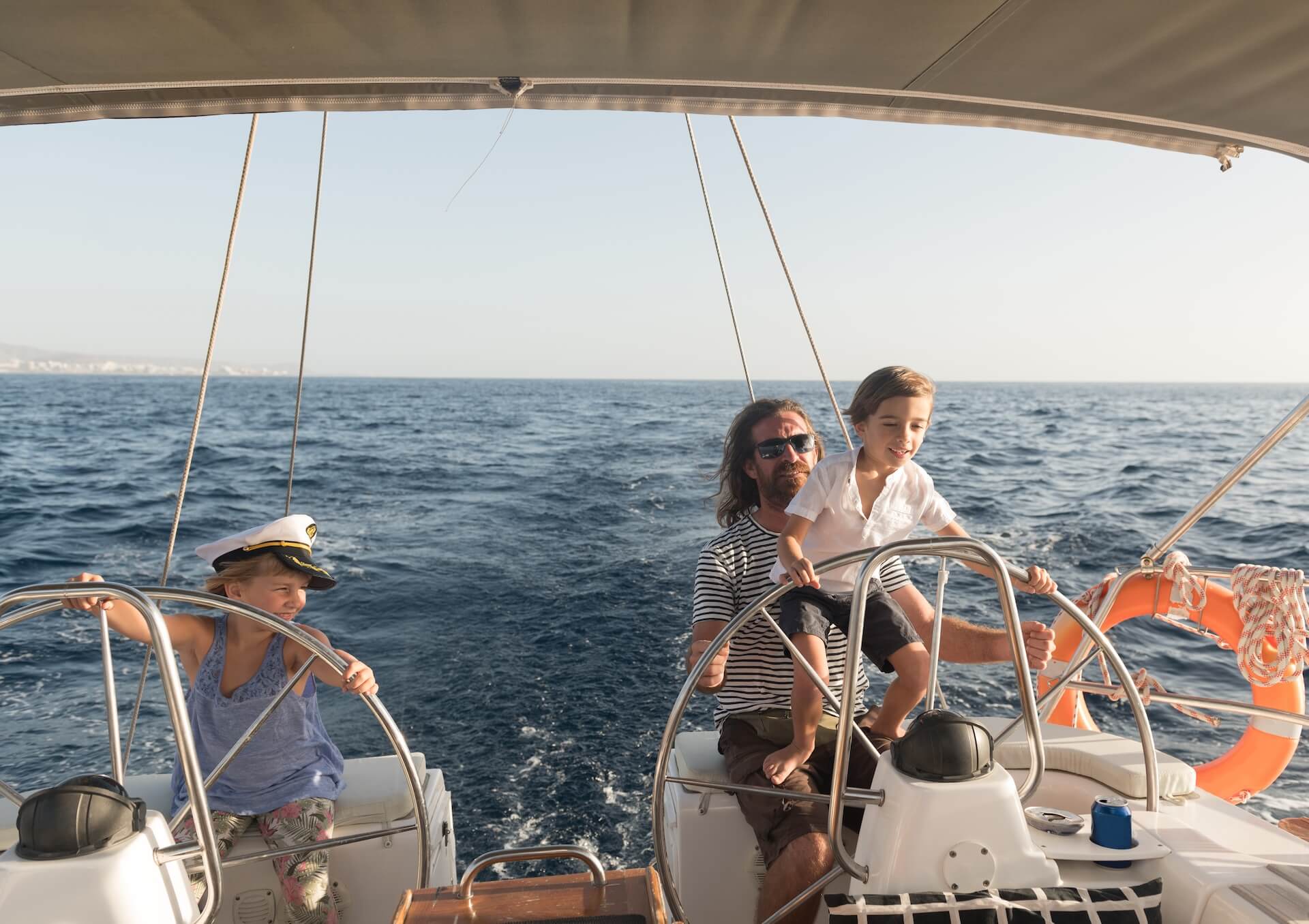 man with boy and girl yacht steering wheel